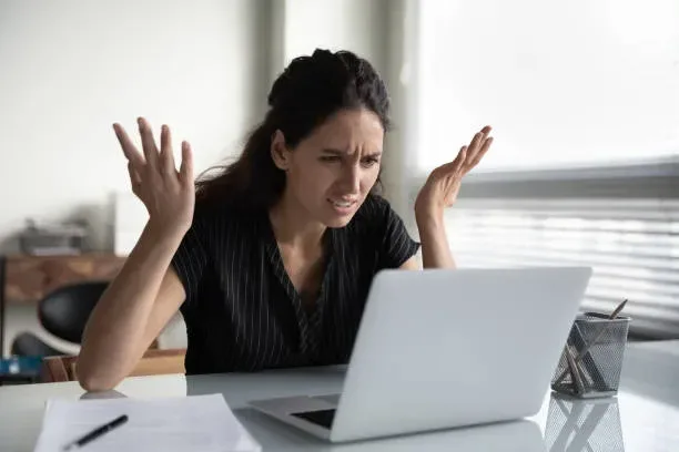 Frustrated businesswoman throwing hands up in stress while looking at laptop screen due to SEO ranking drops.